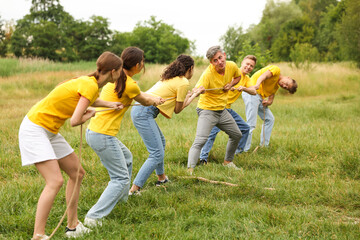 Team building. Group of happy people playing tug of war with rope outdoors