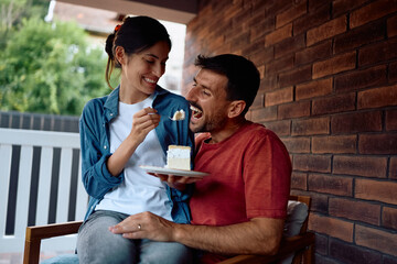 Carefree couple sharing piece of cake on porch.