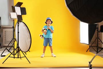 Little boy with penny board on yellow background in photo studio with professional equipment
