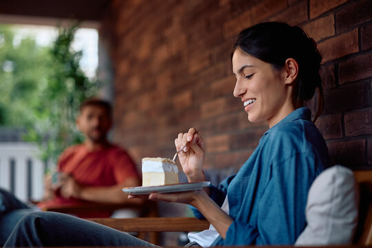Happy woman eating cake while relaxing on porch.