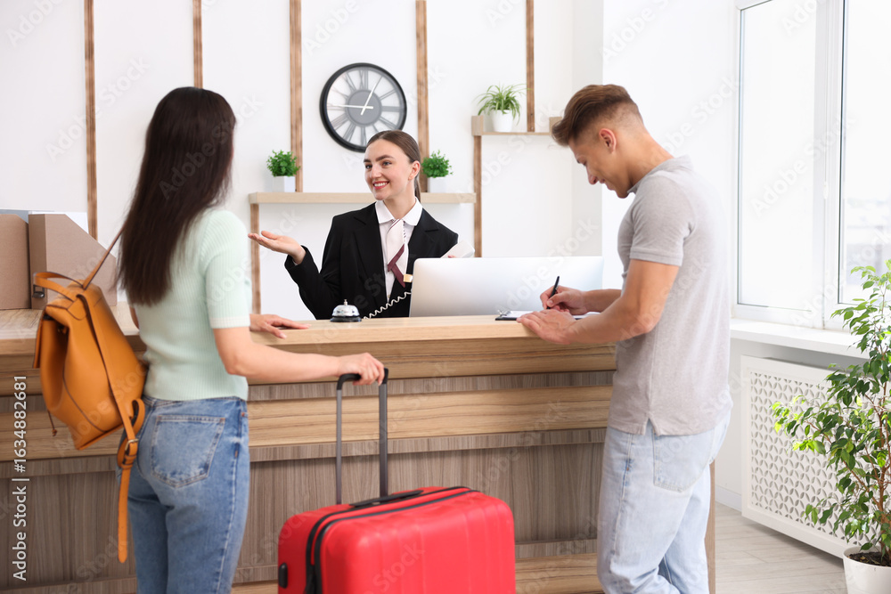 Poster smiling receptionist working with clients at reception desk in hotel