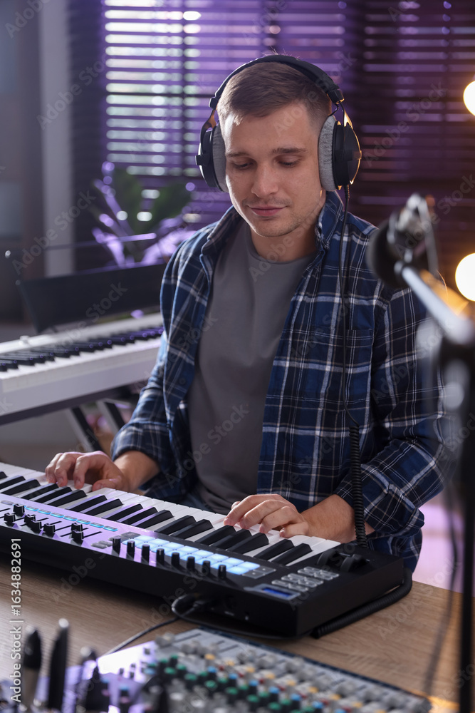 Poster man in headphones working with midi keyboard at table in home studio