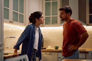 Couple with relationship difficulties looking at each other in kitchen.