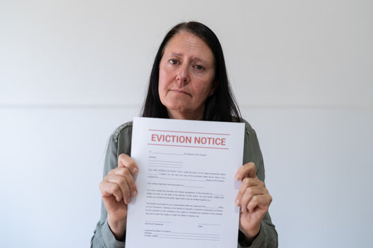 Sad woman looking at the camera and holding an eviction notice. Concept of not paying rent.