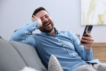 Man with smartphone laughing on sofa at home
