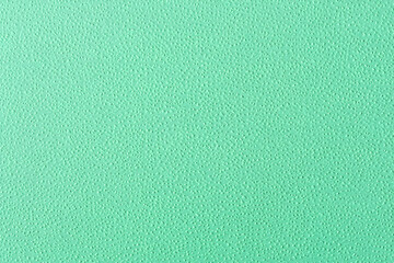 Fototapeta premium Close-up of a mint green textured background. A detailed macro view of a solid pastel surface with a fine, pebbled grain.