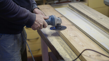 Electric sander used to finish a wooden plank for a smooth texture during crafting. Male hands utilizing a sanding machine on a hardwood in a woodworking setting, demonstrating skilled craftsmanship.