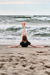 Young woman with light hair practices yoga on baltic sea beach. Waves crash behind her as she performs relaxing pose. Overcast sky and gentle light enhance calm mood