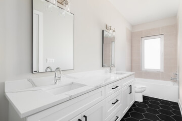A bathroom with a large white cabinet, marble countertop with chrome faucets, brown tiled shower, and black hexagon tile flooring.