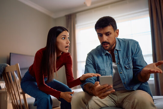 Upset couple arguing about content on cell phone at home.