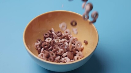 Studio very slo mo slow motion lighting on creamy milk and delicious colorful cereal being poured and falling into breakfast glass bowl with colored background with nutritious break fast morning meal - Powered by Adobe