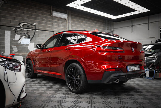 A vibrant red BMW X4 with sleek black rims is parked in a tiled garage with brick walls, overhead grid lighting, and wall mounted equipment.