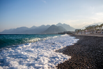 Foamy waves washing over pebble beach with turquoise sea and Taurus Mountains in the background at...