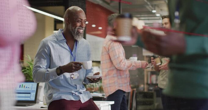 Seated businessman picking coffee mug at laptop sparking chart discussion with colleagues