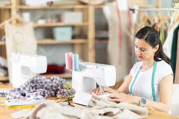 Woman tailor sews clothes in sewing machine. Female worker uses sewing machine to create clothes for clients. Process of making dress in custom workshop studio.