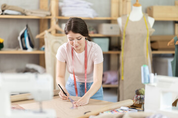 Young female seamstress drawing pattern on paper in sewing workshop