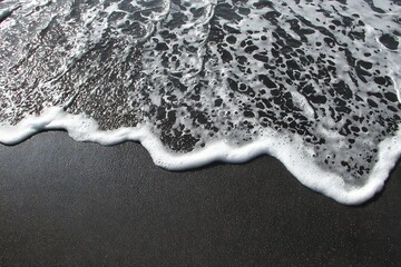 Black sand beach with snowy surf foam  
