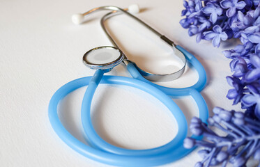 Blue stethoscope looped on white surface with lilac blossoms