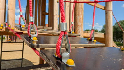 Wooden playground with a suspended rope bridge features red ropes and wooden planks. Ideal for...