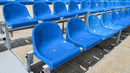 Fototapeta premium Rows of empty blue stadium seats on metal frame under bright sunlight. Ideal for sports, event and spectator themes
