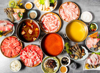 Traditional Hot Pot Feast with Sliced Meats, Seafood, and Vegetables various broths, platters of thinly sliced beef and pork, seafood, vegetables, dipping sauce, and rice on Grey Background top view