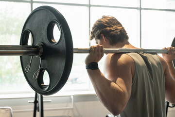 Confident young man exercising with barbell at fitness center. Cross training. Male athlete lifting...