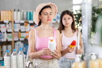 Mother and daughter in summer clothes went to the pharmacy and choose sunscreen and SPF for a trip to the beach. Family is going on vacation and choosing a sunscreen