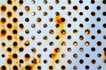Closeup of corroded metal plate texture with numerous round perforated holes and rust details