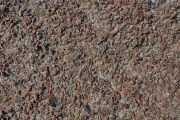Close-up texture of a rough, weathered concrete surface embedded with various sizes of reddish and gray stones.