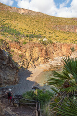 Man walking down trail to hidden rocky beach with clear turquoise sea