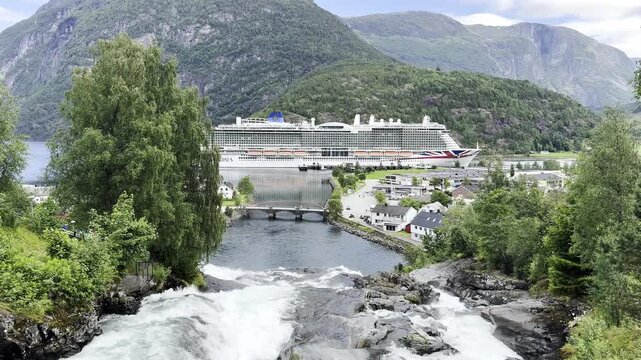 A passenger ship moored in the port of the village of Hellesylt, Norway, with a view of the waterfall