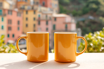 Pair of yellow ceramic mugs mockup placed on a sunny balcony with a charming view of pastel Mediterranean architecture