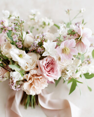 Luxurious pastel-toned wedding bouquet featuring blush roses and seasonal blooms, tied with a silk ribbon