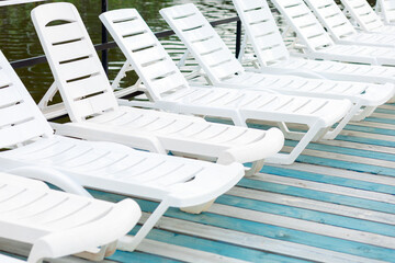 White plastic sun loungers are neatly lined up on a wooden deck by the water. They are perfect for relaxing in the fresh air, creating an atmosphere of coziness and tranquility.