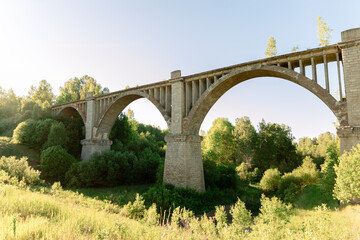 Fototapeta premium A viaduct with stone arches against a bright blue sky at sunset. Old stone bridge in the countryside