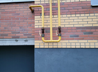 Yellow gas pipes on the wall of a red brick house.