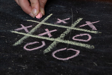 Female hand drawing tic tac toe on black school board with chalk, play