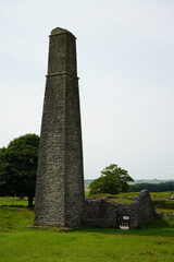 Fototapeta premium Magpie Mine, The Peak District, England – August 6 2025: Tall stone chimney and ruined building in a picturesque summer landscape.