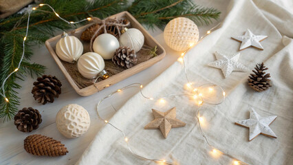 Christmas ornaments, stars and pine cones are arranged on a white surface with string lights, creating a festive and cozy winter holiday scene