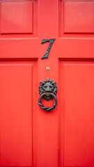 Red front door with number seven. Closeup of house entrance detail with antique black iron lion head door knocker