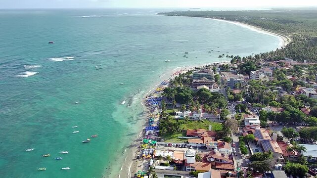 Aerial drone view of the stunning coastline of Porto de Galinhas at Enseadinha Beach in Pernambuco, Brazil. A vibrant tropical town meets the turquoise ocean with boats and tourists on a sunny day.