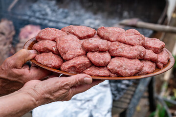 The weathered hands of an experienced person hold a rustic clay plate piled high with fresh, raw...