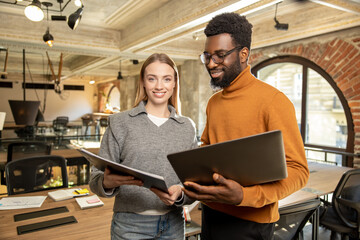 Diverse colleagues discussing project while standing in modern loft office and reviewing document