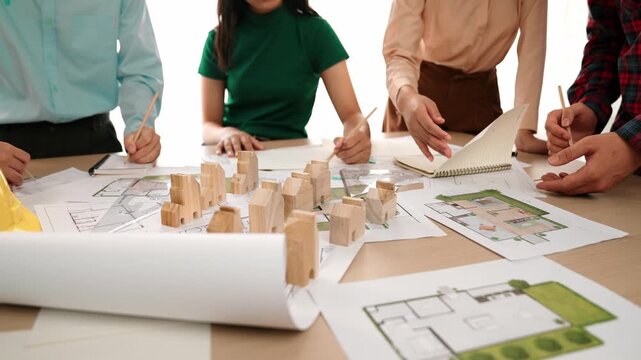 Smart architect and safety engineer discussion about building blueprint on table with architectural document, measurement tools and wooden block scatter around at modern office. Closeup. Delineation.