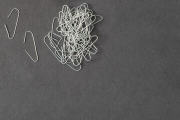 Minimalist office flatlay featuring a pile of silver hook-shaped paper clips scattered over a dark...