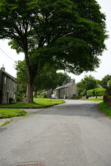 Sheldon, The Peak District, England – August 6 2025: Tranquil village lane featuring historic stone cottages amidst lush greenery.
