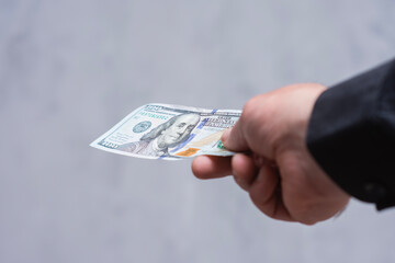 Close-up of a man's hand offering a US one hundred dollar bill. Concept financial transaction,...