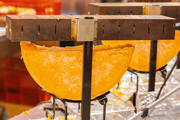 Large wheel of cheese displayed on a stand in a vibrant market setting with colorful background