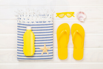 Beach towel with summer accessories on wooden background, top view