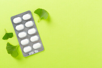 Ginkgo leaf with pills on color background, top view